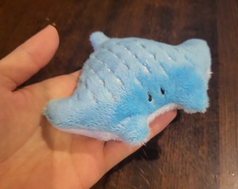 May include: A small, light blue plush manta ray with a white belly and silver glitter accents.