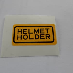 May include: A yellow rectangular sticker with black text that reads "HELMET HOLDER".