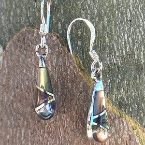 May include: A pair of silver dangle earrings with teardrop-shaped abalone shell inlays. The shell has a brown, green, and iridescent blue color.