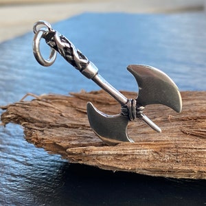 Könnte beinhalten: Ein silberner Axtanhänger mit einem geflochtenen Griff. Die Axt hat zwei Klingen und ist ein beliebtes Symbol für Stärke und Macht.