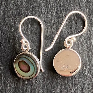 Peut inclure: Une paire de boucles d'oreilles en argent avec un pendentif rond en nacre d'ormeau. L'arrière de la boucle d'oreille est en argent avec le numéro 925 estampillé dessus.