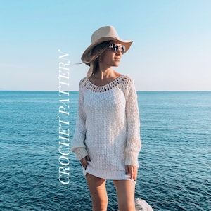 Puede incluir: Un vestido de punto de ganchillo blanco con cuello de ganchillo y mangas largas. La modelo lleva un sombrero de paja y botas blancas. El fondo es un oc&eacute;ano azul y una costa rocosa.