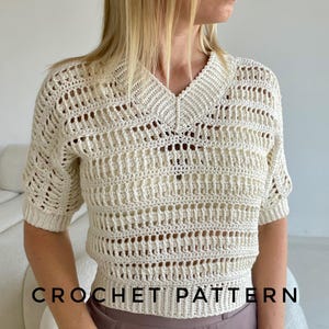 May include: A crochet top with a V-neck and short sleeves. The top is made with white yarn and has a delicate openwork pattern. The text "CROCHET PATTERN" is visible at the bottom of the image.