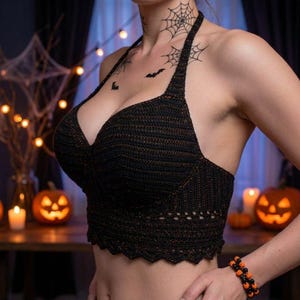Peut inclure: Un haut dos nu en crochet noir avec une encolure en cœur et un ourlet festonné. Le vêtement est réalisé avec un motif de points texturés et comprend un bracelet composé de perles sphériques noires et orange alternées au poignet.