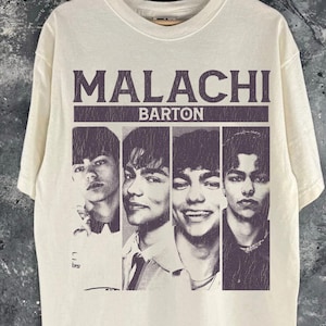 May include: Off-white t-shirt with the text "MALACHI BARTON" above four black and white portraits. The shirt is a Gildan Activewear 5000, with a note indicating it fits up 2-3 sizes for an oversized fit. The t-shirt is hanging on a wooden hanger.