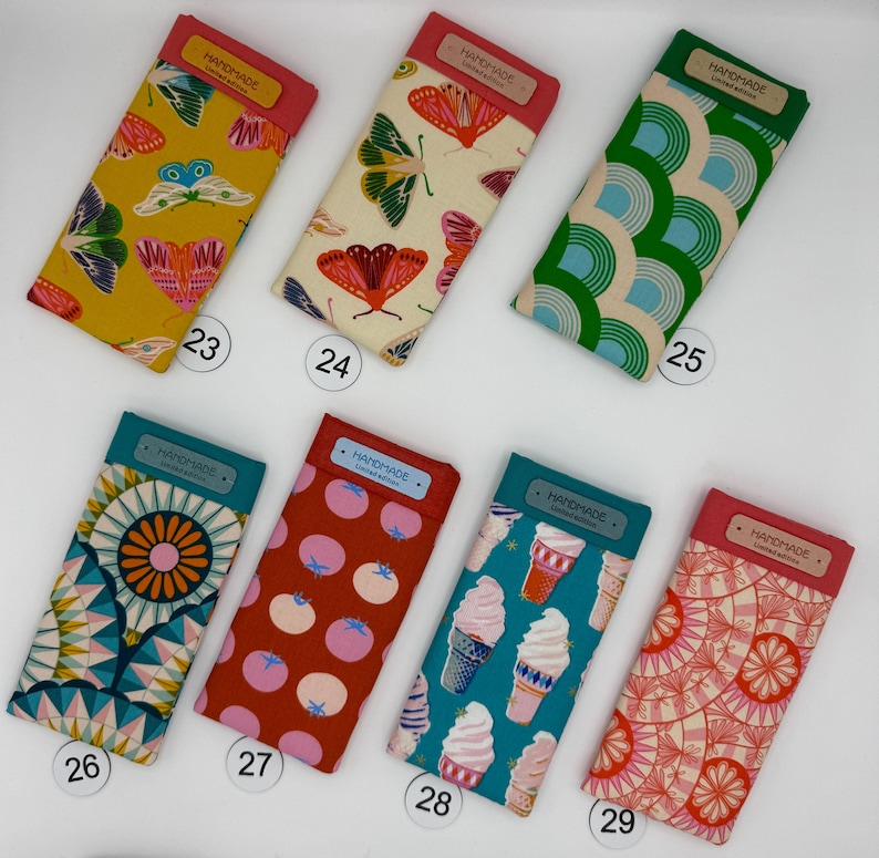 May include: A collection of eight rectangular fabric cases with various patterns. Designs include butterflies, geometric shapes, and ice cream cones. Each case has a colored top and a "HANDMADE" label.