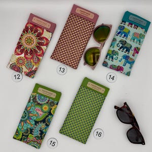 May include: A collection of handmade eyeglass cases in various patterns and colors. Designs include floral, geometric, and elephant prints. Some cases have the word "HANDMADE" on them. Sunglasses are also included.