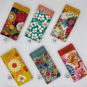 May include: Six handmade fabric glasses cases with floral patterns. Each case has a rectangular shape with a contrasting top flap. The cases feature various designs, including large flowers, daisies, and tropical leaves. The cases are numbered 17, 18, 19, 20, 21, and 22.