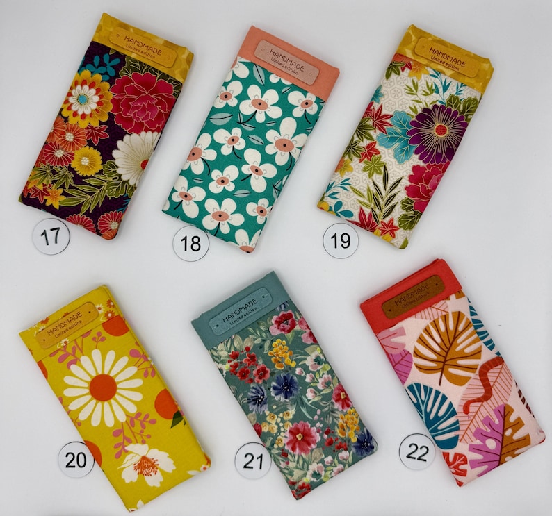 May include: Six handmade fabric glasses cases with floral patterns. Each case has a rectangular shape with a contrasting top flap. The cases feature various designs, including large flowers, daisies, and tropical leaves. The cases are numbered 17, 18, 19, 20, 21, and 22.