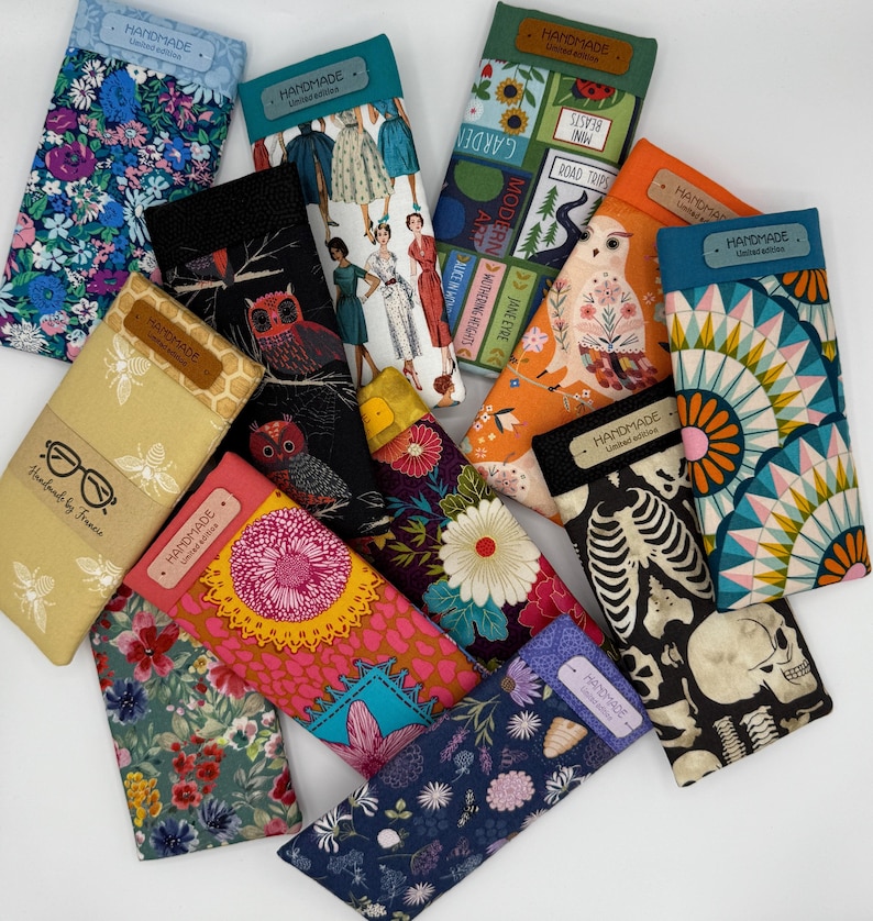 May include: A collection of handmade glasses cases with various fabric patterns. Designs include floral, owl, skeleton, and vintage dress prints. Each case has a label that says "HANDMADE". Some cases have text that says "Handmade by France".