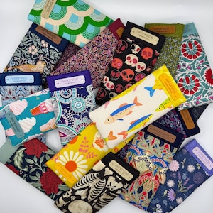Puede incluir: Una colección de estuches rectangulares de tela con diversos patrones, incluyendo calaveras, peces, flores, cachemir y diseños geométricos. Cada estuche tiene una etiqueta rectangular que dice HANDMADE Limited edition.