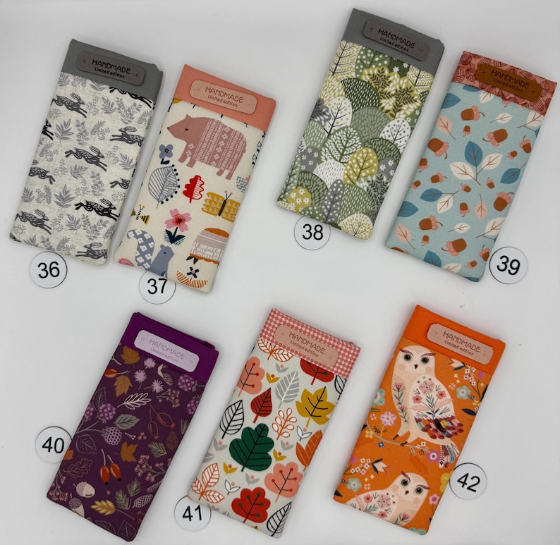 May include: A collection of handmade glasses cases with various fabric patterns. Designs include rabbits, bears, trees, leaves, and owls. Each case has a rectangular shape with a top flap labeled "HANDMADE Limited Edition".