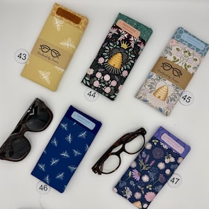 May include: A collection of handmade eyeglass cases in various patterns and colors. Designs include bees, floral, and insect motifs. Each case has a label that says "HANDMADE" and "Handmade by Francie".