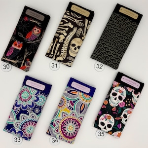 May include: A collection of six eyeglass cases with various designs. The cases feature patterns including owls, skeletons, a black wave pattern, and floral designs with skulls. Each case has a rectangular shape with a dark top and a label that reads "HANDMADE Limited Edition."