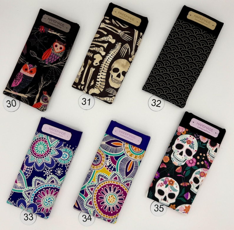 May include: A collection of six eyeglass cases with various designs. The cases feature patterns including owls, skeletons, a black wave pattern, and floral designs with skulls. Each case has a rectangular shape with a dark top and a label that reads "HANDMADE Limited Edition."