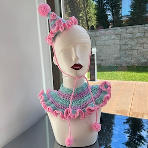 May include: A pink and green crocheted collar with a ruffled edge and a matching pink and green crocheted hat with a pom-pom on top.