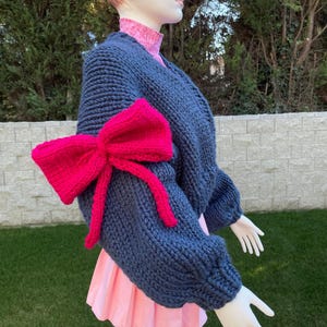 May include: A dark blue knitted cardigan with a large pink bow on one sleeve.