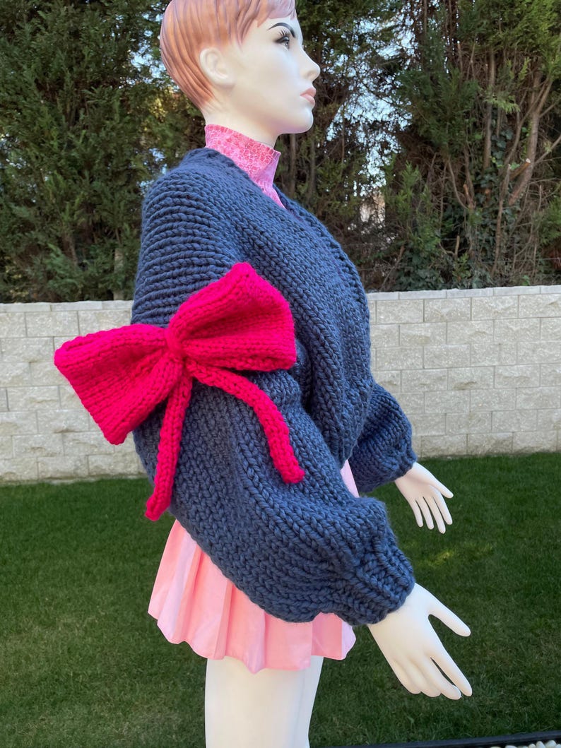 May include: A dark blue knitted cardigan with a large pink bow on one sleeve.