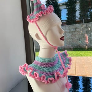 以下が含まれることがあります： 帽子と襟のセット。ピンクとグリーンの糸で編まれた、ポンポン付きのクラウン型の帽子と襟。