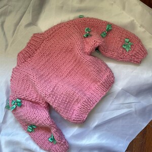 May include: A pink knitted sweater with green bows on the sleeves.