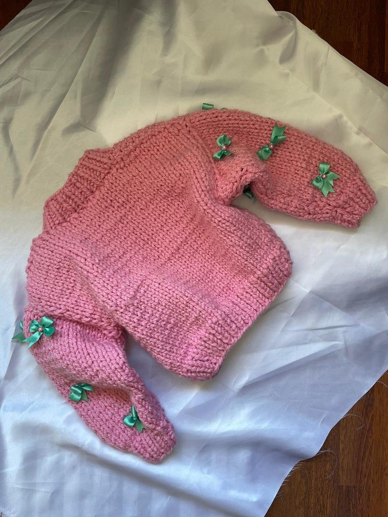 May include: A pink knitted sweater with green bows on the sleeves.