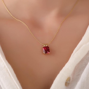 Może przedstawiać: Złoty łańcuszek z czerwonym kwadratowym wisiorkiem.