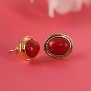 May include: A pair of gold stud earrings with red oval-shaped stones.