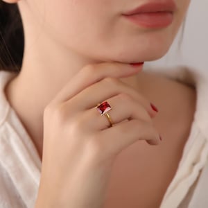 May include: A gold ring with a square-shaped red gemstone.