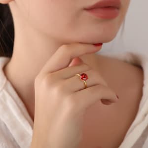 Può includere: Un anello d'oro con una pietra preziosa rossa. L'anello è al dito di una persona.