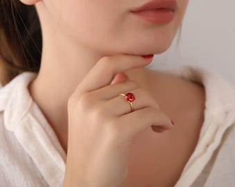 May include: A gold ring with a red gemstone. The ring is on a person's finger.