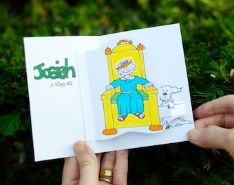 Könnte beinhalten: Eine Pop-up-Karte mit einer grünen Illustration des Namens Josiah und dem Text "2 Könige 22". Die Karte ist geöffnet, um eine Pop-up-Illustration eines jungen Jungen zu zeigen, der eine Krone trägt und auf einem gelben Thron sitzt.