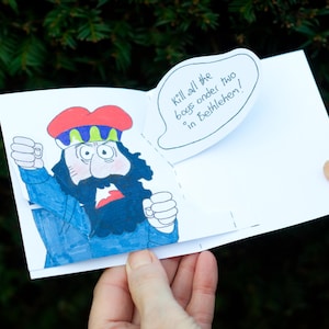 May include: A pop-up card with a cartoon illustration of a man wearing a red hat and blue clothing. The speech bubble says, "Kill all the boys under two in Bethlehem!"