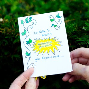 May include: A white card with green vines and a yellow sunburst. The card says "Our Father in heaven hallowed be your name your Kingdom come..."
