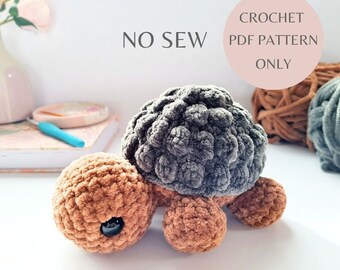 May include: A small, handmade crochet tortoise in shades of brown and gray. The tortoise has a textured shell and body, with a black eye. The image includes the text "NO SEW" and "CROCHET PDF PATTERN ONLY". The words "SMALL TORTOISE" are also visible.