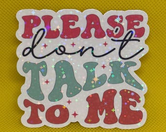 May include: A white sticker with a glittery finish. The sticker says "Please don't talk to me" in a retro font. The words "Please" and "to me" are in red, "don't" is in black, and "talk" is in green.
