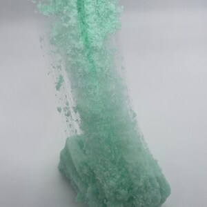 May include: A light green slime with a glittery texture. The slime is being stretched and pulled, revealing its stringy consistency.