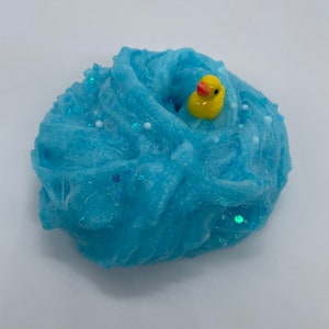 May include: Blue slime with white and iridescent glitter, a yellow rubber ducky is partially submerged in the slime.