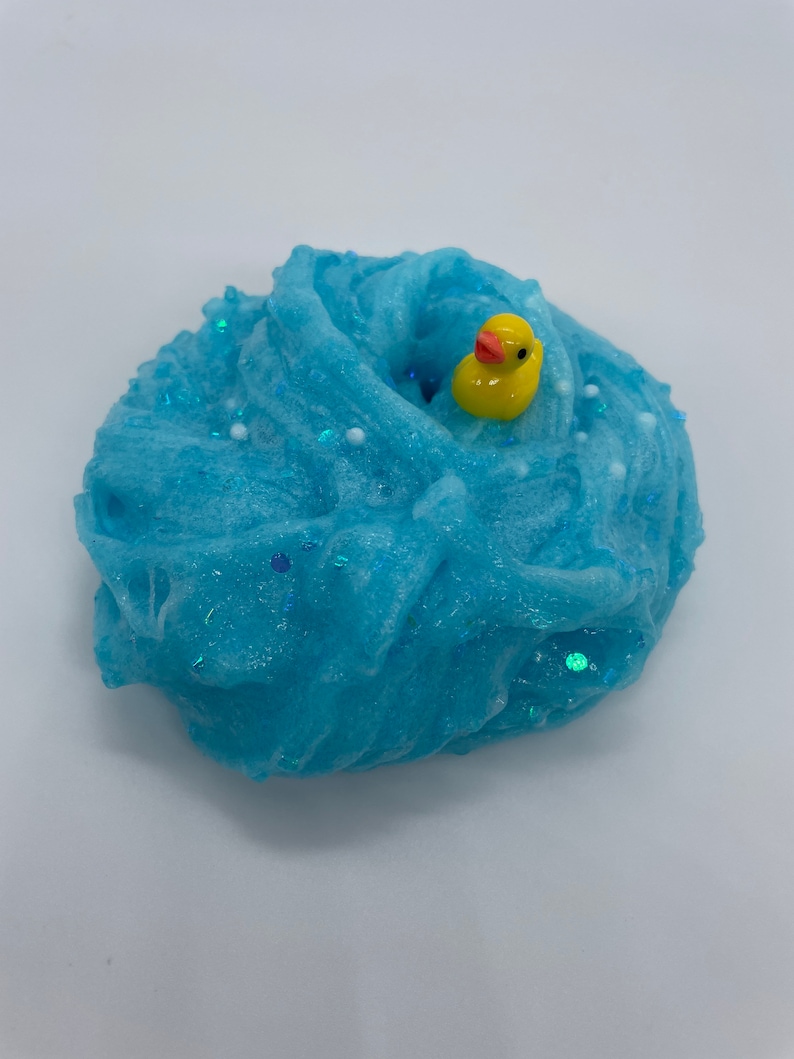 May include: Blue slime with white and iridescent glitter, a yellow rubber ducky is partially submerged in the slime.
