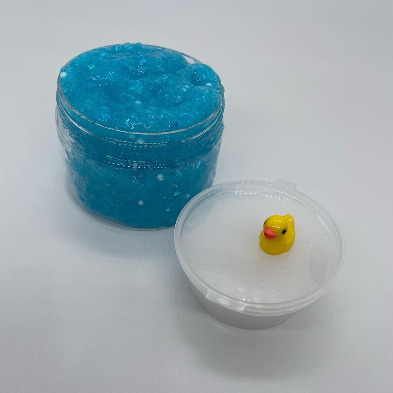 May include: A clear plastic container filled with light blue slime with white glitter. The container has a lid with a small yellow rubber ducky on top.