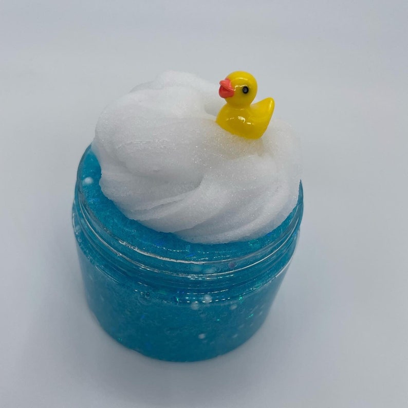 May include: A clear jar filled with blue slime with white glitter and a white fluffy cloud slime on top. A yellow rubber ducky sits on top of the cloud slime.