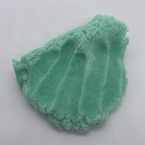 May include: A close-up of a light green, glittery slime. The slime is textured and has a slightly rough surface.