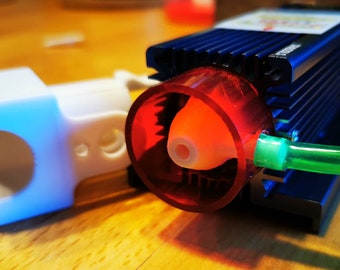 May include: A close-up of a small, blue water pump with a red plastic impeller and a green hose attached. The pump is mounted on a white plastic base.