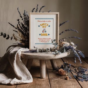 May include: A framed sign with a blue and yellow design that says "Please help us color Baby's 1st Book. Choose a letter to color and sign your name. Thank you!"