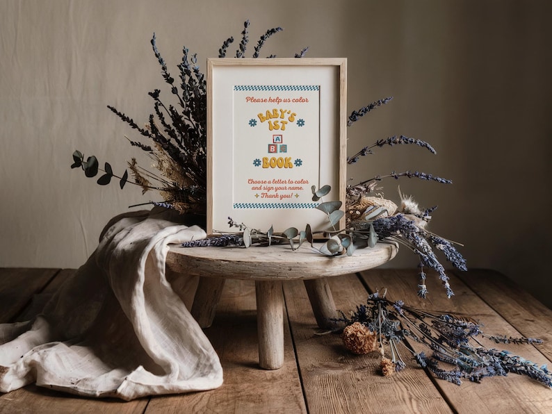 May include: A framed sign with a blue and yellow design that says "Please help us color Baby's 1st Book. Choose a letter to color and sign your name. Thank you!"