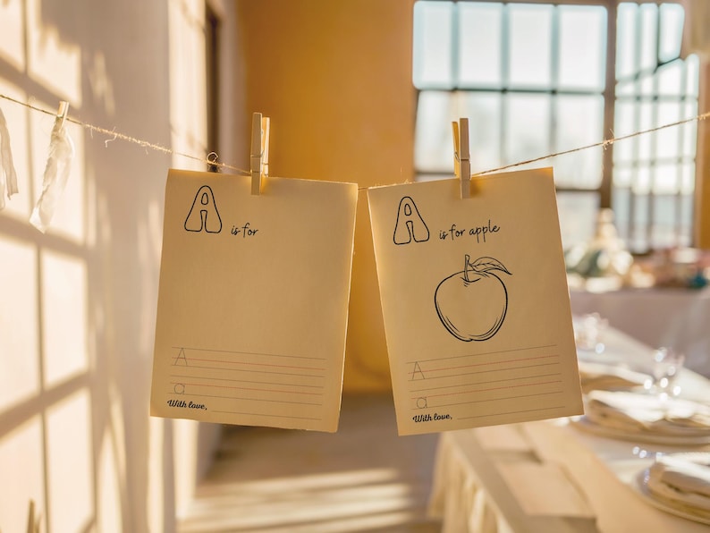 May include: Two blank cards with clothespins hanging from a string. The cards are beige and have the letter "A" written on them. One card says "A is for apple" and has a drawing of an apple. The other card says "A is for" and has a blank line for writing.