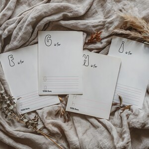 May include: Four blank white cards with handwritten letters and the phrase "is for" on each card. The letters are G, F, H, and I. The cards are on a beige fabric background.
