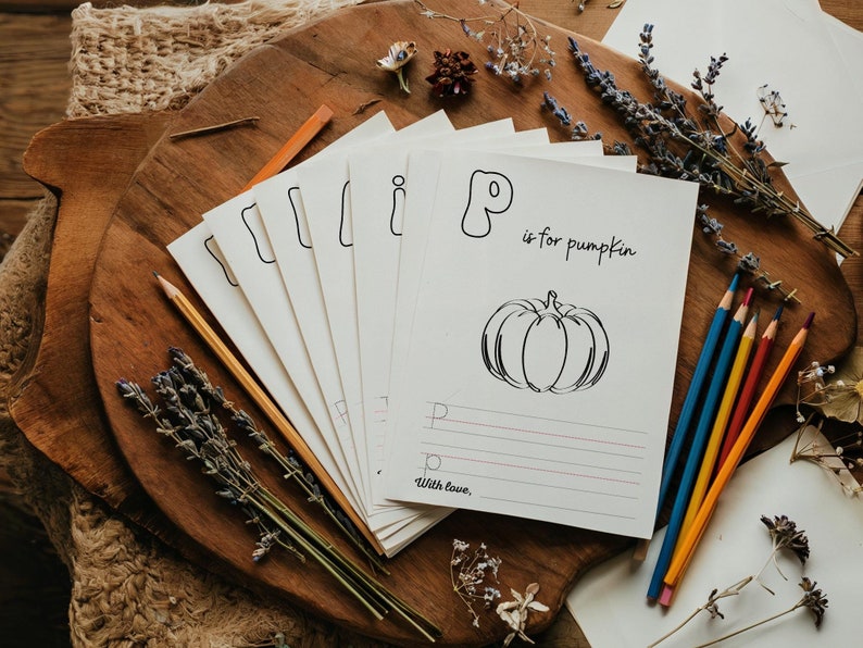 May include: A set of printable alphabet flashcards with a black and white illustration of a pumpkin and the text "P is for pumpkin". The cards are on a wooden surface with dried lavender and colored pencils.