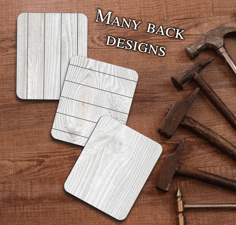 May include: Three white wood coasters with a wood grain pattern. The coasters are on a brown wood surface. The text "MANY BACK DESIGNS" is written in black letters on the surface.