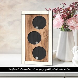 Peut inclure: Une décoration murale en bois avec trois découpes circulaires. Le bois est teinté d'une couleur brun clair et a une bordure blanche. Les découpes sont noires avec un cercle blanc au centre.