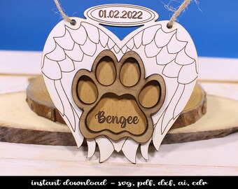 Op de afbeelding: Wit houten hartvormig ornament met een uitgestanste voetafdruk en engelenvleugels. De voetafdruk heeft de naam "Bengee" erin gegraveerd en de datum "01.02.2022" staat op de halo boven het hart.